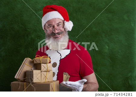 Mature bearded man wearing Santa hat with many gifts in hand, Santa smiling and looking at camera, copy space 71434281