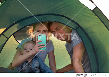 Young family with small child in camping tent taking photo on phone. Young family with small child in camping tent taking photo on phone. 71435865