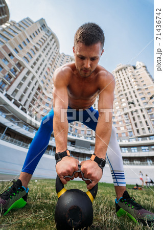 Sportive guy training with kettlebell on the background of a tall building. Sportive guy training with kettlebell on the background of a tall building. 71436742