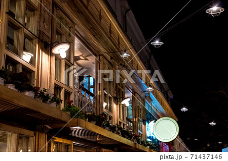 wooden facade of a romantic restaurant in Italian style with windows and flowerpots, night scene with lighting lanterns, nobody. 71437146