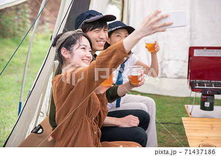 キャンプ場でビールを飲みながらスマホを使うアジア人男女 71437186