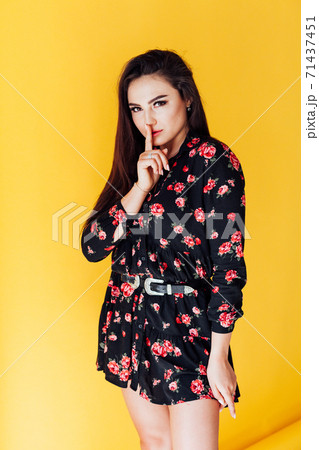 Beautiful fashionable brunette woman in a dress with flowers finger at the lips 71437451