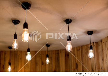 many edison bulbs hanging on a white ceiling in a room with wooden walls, retro style electric lighting in an eco friendly interior close-up of glow details, nobody. 71437532