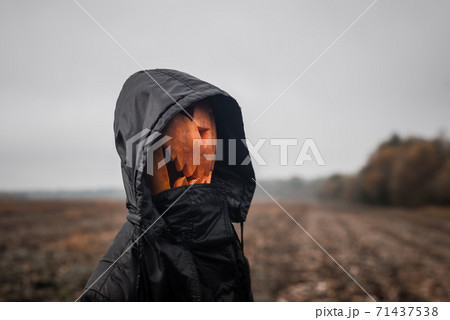 A pumpkin-headed figure Halloween jack-o'-lantern with a scary face in a black hooded robe stands in the  field 71437538