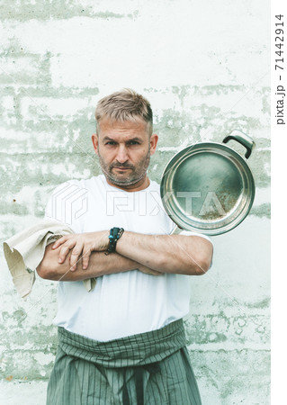 Stylish chef in an apron and with a steel frying pan on a brick wall background. Vertical shot 71442914