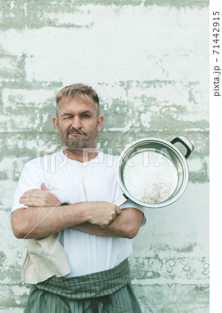 Stylish caucasian attractive chef in an apron and with a steel frying pan on a brick wall background. Vertical shot 71442915