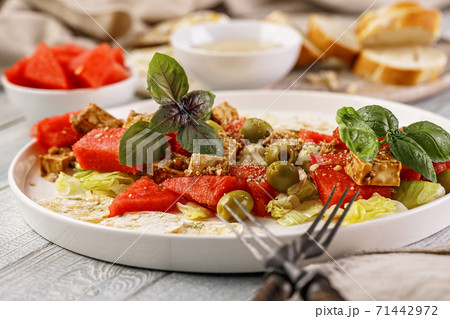 Close-up healthy and tasty vegan salad with watermelon, olives, fresh herbs, basil, multi-grain chips and peanut sauce. Vegetarian food. 71442972