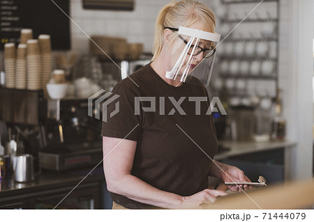 Waitress wearing face mask working in a cafe. 71444079