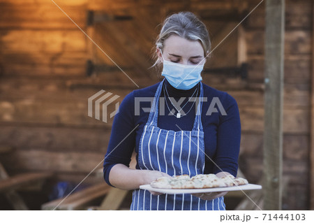 Woman waitress in apron and face mask holding plate of pizza. 71444103