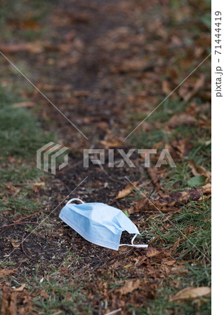 High angle close up of disposed blue surgical face mask lying on ground. High angle close up of disposed blue surgical face mask lying on ground. 71444419