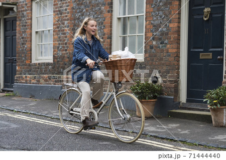 Young blond woman cycling down a village street. Young blond woman cycling down a village street. 71444440