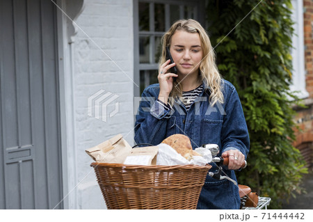 Young blond woman on bicycle with basket, talking on mobile phone. Young blond woman on bicycle with basket, talking on mobile phone. 71444442