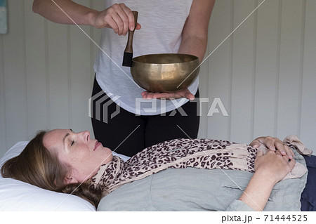 Woman on a couch, and a female therapist using Tibetan singing bowl, sound therapy 71444525