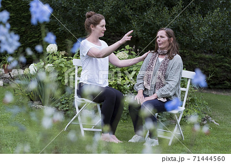 Woman and female therapist seated at an alternative therapy session in a garden. 71444560