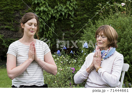Woman and female therapist seated in a garden, hands together and eyes closed. Woman and female therapist seated in a garden, hands together and eyes closed. 71444661