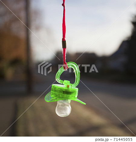 A green plastic baby pacifier dangling from an orange lanyard A green plastic baby pacifier dangling from an orange lanyard 71445055