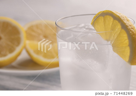 Refreshing cold water with lemon in a wet glass with ice. On a white wooden table. Ready for use. A piece of fruit lies on a white plate. Slimming refreshment drink 71448269