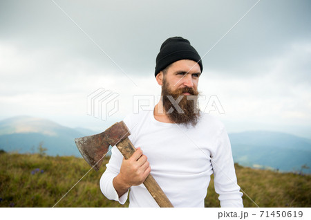 Hipster with beard on strict face holds axe, skyline on background. Lumberjack brutal Hipster with beard on strict face holds axe, skyline on background. Lumberjack brutal 71450619