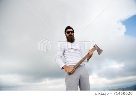 Hipster with beard on strict face holds axe, cloudy sky background. Man with beard Hipster with beard on strict face holds axe, cloudy sky background. Man with beard 71450620