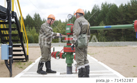 Two oil field technical workers closing valve of x-mass wellhead to shut off well. Decline in oil production after adoption of agreements at meeting of OPEC to stabilize price of oil. 71452287