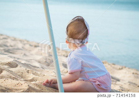 Little girl child in summer dress sits on beach beach or sea and lake and playing with yellow sand Little girl child in summer dress sits on beach beach or sea and lake and playing with yellow sand 71454158
