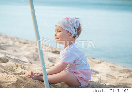 Little girl child in summer dress sits on beach beach or sea and lake and playing with yellow sand	 71454162