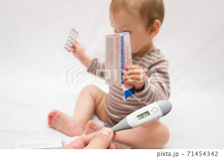 hand holds a thermometer with a high temperature on a white isolated background child with pills hand holds a thermometer with a high temperature on a white isolated background child with pills 71454342