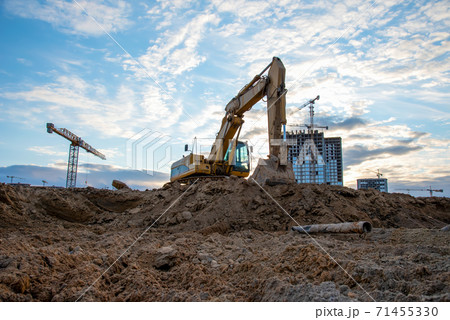 Excavator during earthmoving at construction site on sunset background. Excavator during earthmoving at construction site on sunset background. 71455330