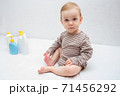 beautiful baby holding a bottle in the hand with shower gel, beside lies Baby cosmetic tubes on white isolated background 71456292