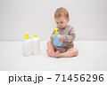 beautiful baby holding a bottle in the hand with shower gel, beside lies Baby cosmetic tubes on white isolated background 71456296