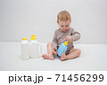 beautiful baby holding a bottle in the hand with shower gel, beside lies Baby cosmetic tubes on white isolated background 71456299