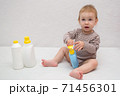 beautiful baby holding a bottle in the hand with shower gel, beside lies Baby cosmetic tubes on white isolated background 71456301