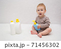 beautiful baby holding a bottle in the hand with shower gel, beside lies Baby cosmetic tubes on white isolated background 71456302