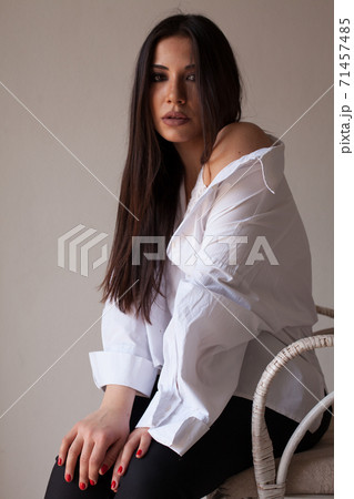 Beautiful fashionable brunette woman in a white shirt sits on a chair Beautiful fashionable brunette woman in a white shirt sits on a chair 71457485
