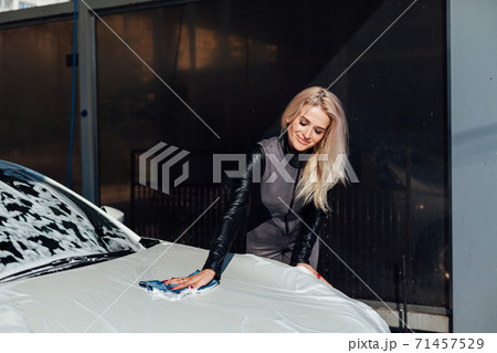 Beautiful blonde woman washes white car foam at car wash 71457529