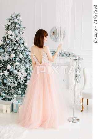 New Year party, Christmas, holidays, people and celebration concept. Back full length view of pretty sexy woman in evening dress standing over christmas tree and decorations background New Year party, Christmas, holidays, people and celebration concept. Back full length view of pretty sexy woman in evening dress standing over christmas tree and decorations background 71457593