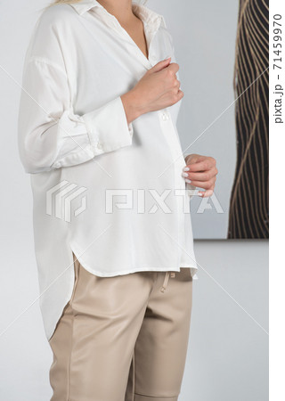 Stylish beautiful young blond woman in a tight biege pants and white shirt near a white wall in the room. Attractive girl model posing. 71459970