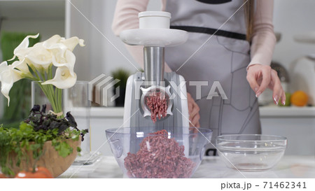 Woman puts pieces of raw meat into electric meat grinder. Pile of chopped meat. Electric mincer machine with fresh chopped meat. Preparation of minced beef with an electric meat grinder. Woman puts pieces of raw meat into electric meat grinder. Pile of chopped meat. Electric mincer machine with fresh chopped meat. Preparation of minced beef with an electric meat grinder. 71462341