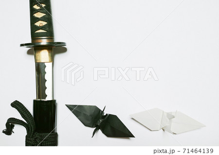 白い紙の左端に配置した抜きかけの日本刀と下に配置した黒と白の折り鶴の写真素材