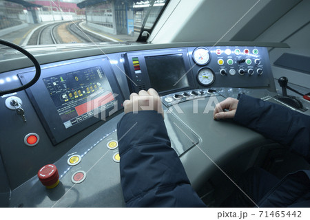 At the cabin of the passenger train. Train driver sitting in front of the dashboard and putting hand on start lever At the cabin of the passenger train. Train driver sitting in front of the dashboard and putting hand on start lever 71465442