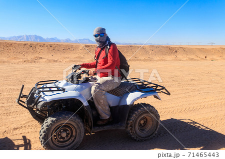 Young man in safari trip through egyptian desert driving ATV. Quad bikes safari in the desert near Hurghada, Egypt Young man in safari trip through egyptian desert driving ATV. Quad bikes safari in the desert near Hurghada, Egypt 71465443