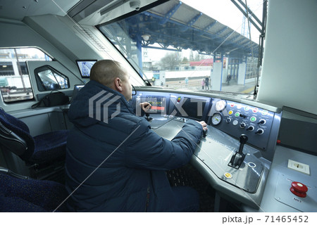Train driver sitting in the cabin of the passenger train in front of the dashboard 71465452