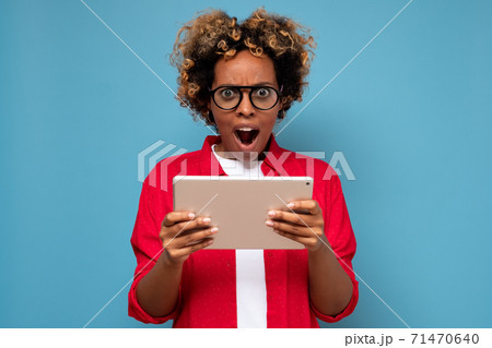 Young african curly woman shocked by news displayed on a digital tablet. Young african curly woman shocked by news displayed on a digital tablet. 71470640