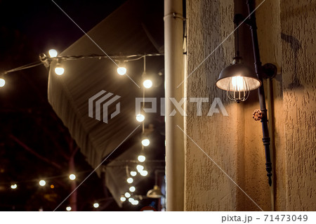 retro loft style street lantern on a building facade illuminates a city street at night, a closeup of a designer edison lamp with valve and garland light bulbs. 71473049