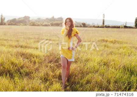 Beautiful woman in yellow dress walks on the field with flowers 71474316