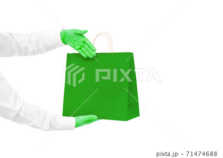 hands in green sterile gloves of faceless courier for safe delivery of eco food in green package shows palm at packet during quarantine of social distance isolated on white with copy space. hands in green sterile gloves of faceless courier for safe delivery of eco food in green package shows palm at packet during quarantine of social distance isolated on white with copy space. 71474688