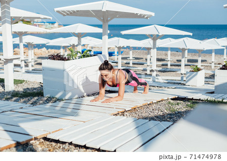 Beautiful fashionable brunette woman does fitness yoga on the beach by the sea 71474978