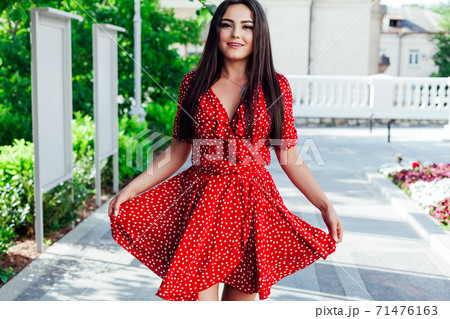 Beautiful fashionable brunette woman in a red summer dress walks in the street 71476163