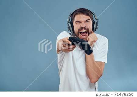 Man in headphones controller in hands playing game console lifestyle emotions blue background white t-shirt 71476850