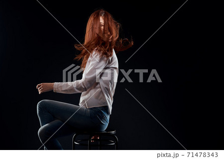 pretty woman sitting on a chair posing white shirt jeans long hair red lips dark background 71478343